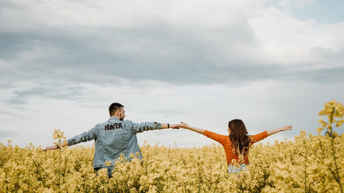 A couple enjoying a warm summer day in a vibrant yellow flower field, radiating joy and freedom.